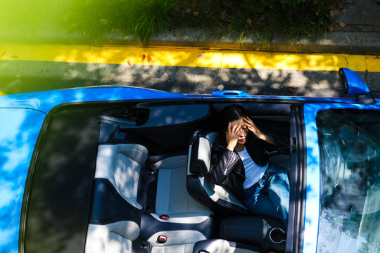 A stylish Asian girl sleeps inside a blue convertible.