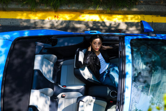 A stylish Asian girl sleeps inside a blue convertible.