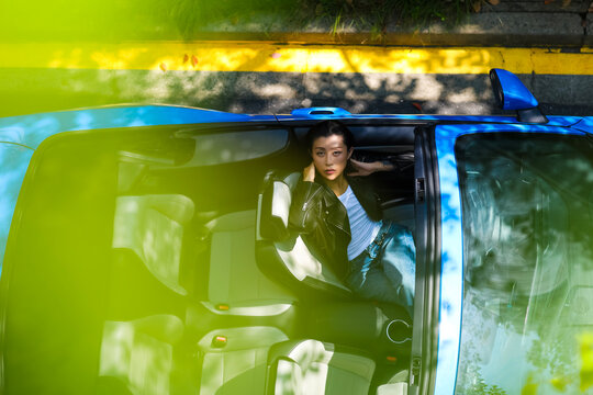 A stylish Asian girl sleeps inside a blue convertible.