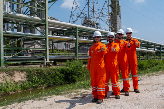 Workers in safety gear at an industrial site point towards the camera during a sunny day