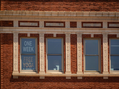 Historic red brick facade with ornate white trim pilasters and window advertising a free week of yoga on a sunny summer day