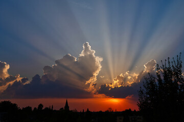 Fototapeta premium sunset with the silhouette of a church and dramatic, colorful cumulus clouds with sunbeams over Ratingen Homberg 