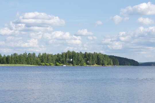 Forested green island in the middle of a calm blue lake under a cloudy sky in Finland