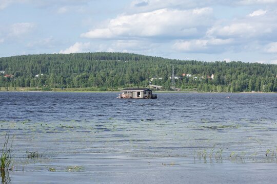Floating sauna boat on a calm lake with a forested hill in Finland