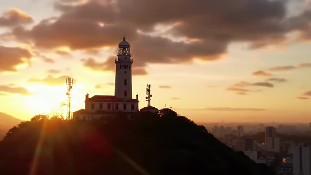 Silhouette of a lighthouse and radio towers against a dramatic sunset over a city.
