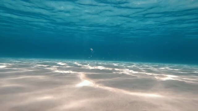 Underwater view of a sandy ocean floor with sun rays filtering through the turquoise water.