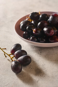 fresh dark purple grapes in bowl on grey textured surface, ripe sweet fruit cluster with stems, in close-up view with soft focus and copy space, healthy organic snack