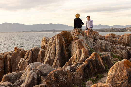 two boys exploring and hiking the spectacular rocky coastline of DeKelders, South Africa at sunset