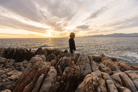 young boy exploring and hiking the spectacular rocky coastline of DeKelders, South Africa at sunset