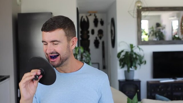 Smiling adult man applying blue teeth whitening strips