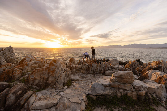 two boys exploring and hiking the spectacular rocky coastline of DeKelders, South Africa at sunset