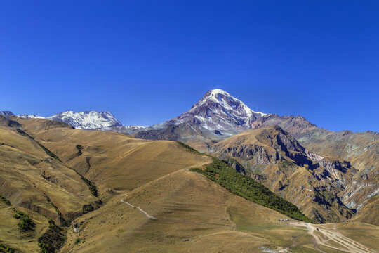Snow covered Mount Kazbek rises in the Caucasus mountains, Georgia. Distant view under blue sky on sunny autumn day