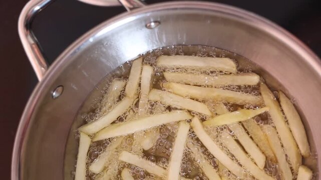 Close-up video of French fries deep frying in hot cooking oil, golden potato strips bubbling in a pan during food preparation in a commercial kitchen.z