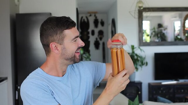 Hungry adult male opening jar eating preserved sausage