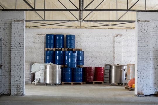 In the center of the room, stacks of blue and red metal barrels are compactly placed on wooden pallets, which is typical for the logistics of chemical production.