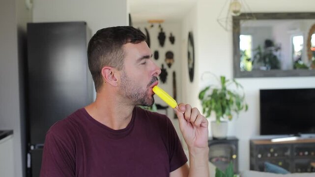 Adult man eating yellow lemon popsicle showing stained tongue
