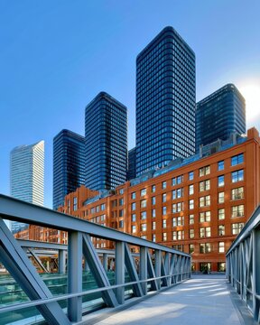 Dynamic urban scene with glass skyscrapers, brick office building and pedestrian bridge in blue light