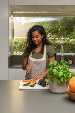 Hispanic woman chopping carrot on cutting board in bright modern kitchen