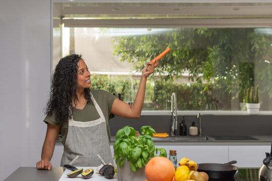 Smiling woman pointing with carrot toward copyspace in kitchen