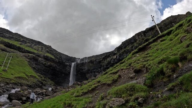 Low angle view of Fossa waterfall with tourist standing by stream, Faroe Islands