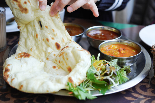 Person tearing freshly baked naan bread with hands to eat with curry at an Indian restaurant