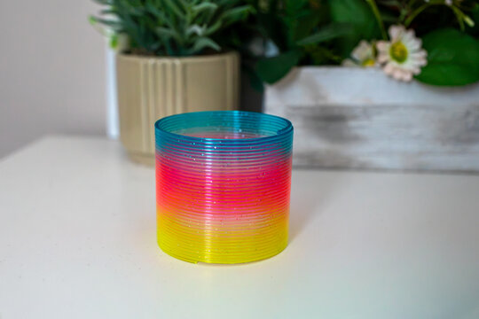 Bright rainbow plastic spring toy expanded into a spiral shape on a white surface. Classic sensory fidget toy showing flexible plastic coils for play, stress relief, tactile interaction and display