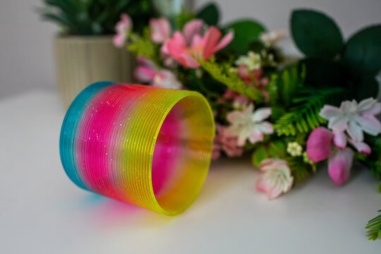 Bright rainbow plastic spring toy expanded into a spiral shape on a white surface. Classic sensory fidget toy showing flexible plastic coils for play, stress relief, tactile interaction and display