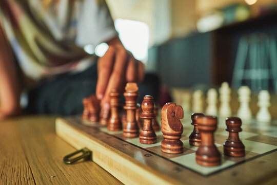 Wooden chess pieces in sharp focus with a hand reaching to play