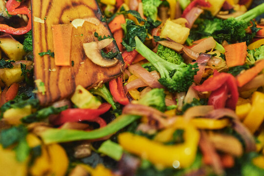 Fresh vegetables cooking in a hot pan with a wooden spoon