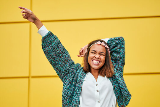 Enthusiastic young woman pointing and smiling against yellow wall