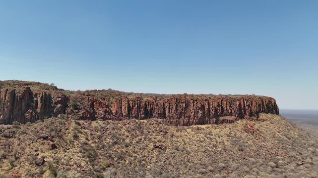 Cinematic aerial footage of majestic red sandstone cliffs and rugged escarpments in the arid wild savanna of Namibia, Africa. Epic geological formations.