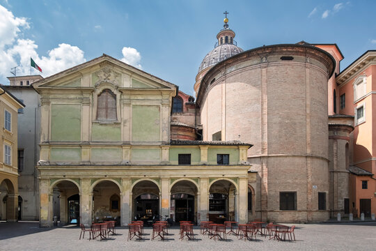 A panoramic view of Piazza San Prospero in Reggio Emilia, Italy, showing the historic Palazzo dei Canonici with its elegant arched portico. The dome and main apse of the Cathedral are also visible.