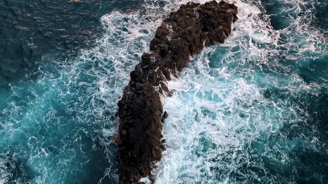 Aerial view of ocean waves crashing against a rock formation