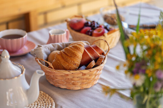 A basket of buns and croissants on a wooden rustic table. The concept of a rural quiet life. Slow lifestyle concept