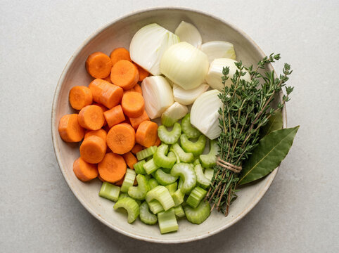 Chopped raw carrots celery onions and herbs in a ceramic bowl