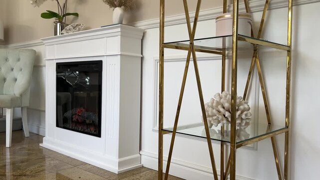 Horizontal 4K video of a luxury glamour style living room featuring a handmade white electric fireplace and a gold shelving unit