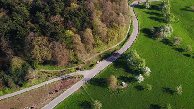 Aerial bird's-eye view of an idyllic rural landscape with a red car driving on a scenic road 