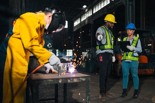 Welder worker factory helmet safety vest spark metal industry engineer team inspecting fabrication process in workshop