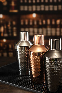 Three shakers sit on a rubber mat against the bar. The shakers are made of copper, steel, and black metal, classic bartender's accessory