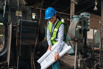 Fototapeta premium Engineer blueprint hardhat factory safety vest woman industry construction worker female engineer holding blueprint in old factory workshop with machinery, planning inspection