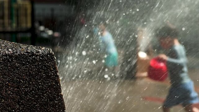 2 boys with pails play in sprinklers on hot Brooklyn  summer day