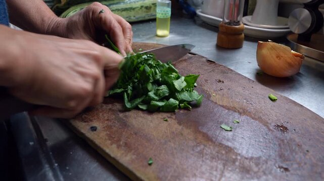 Hands chopping fresh organic spinach on rustic wooden cutting board in artisan kitchen