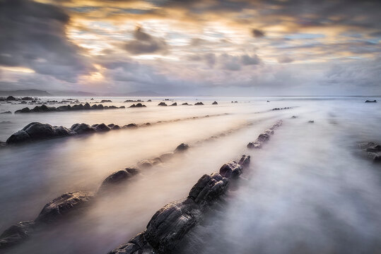 Stunning long exposure sunset at Barrika beach showing silk water flowing between geological flysch rock formations on the Basque coast of Spain