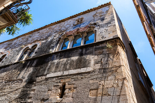 A view from directly below of an ancient Sicilian fortified stone palace, with arched windows reflecting the deep blue of the sky