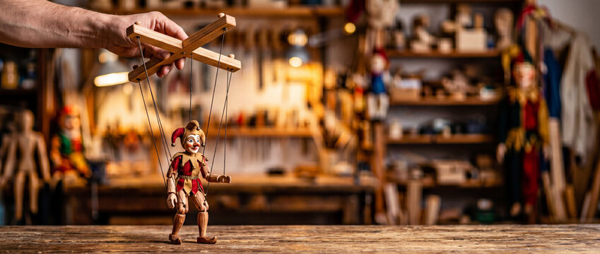 Handheld wooden marionette jester puppet controlled by craftsman in rustic workshop studio