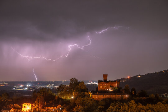 14th-century medieval castle at the top of a hill, captured during a thunderstorm with clear lightning, Castellar, Saluzzo, Bronda Valley, Piedmont, Italy.