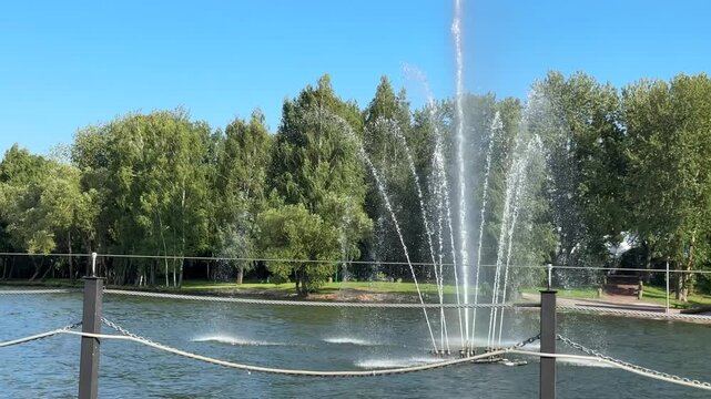 Water fountain in green lakeside park under clear blue sky, blue green infrastructure, urban cooling, climate adaptation and sustainable public space concept.