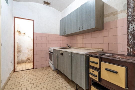 Abandoned kitchen showing old appliances and worn pink tiles