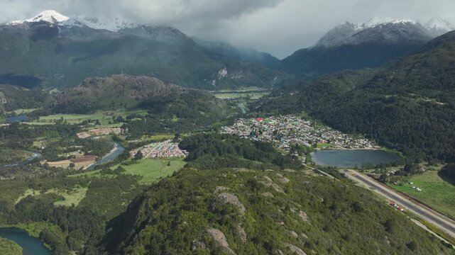 Aerial view of the town of Futaleufu nestled in a valley with a lake and the Futaleufu River, surrounded by rugged snow-capped mountains in Patagonia, Chile.