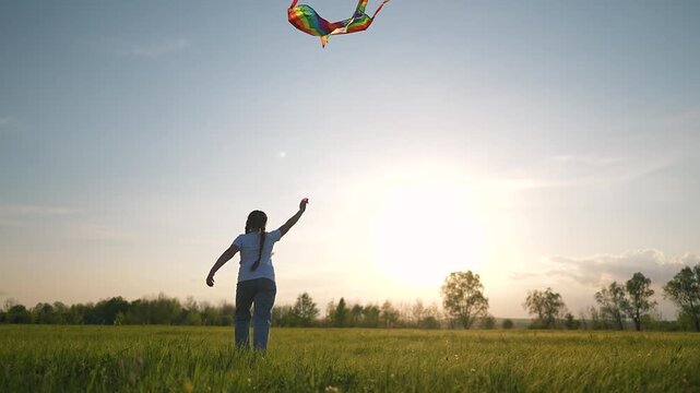 Child gazing toward glowing sunset sky above wide grass field under gentle breeze while absorbing hues. Happy moment unfolds across field as winds stir grasses beneath fading sky backdrop during dusk